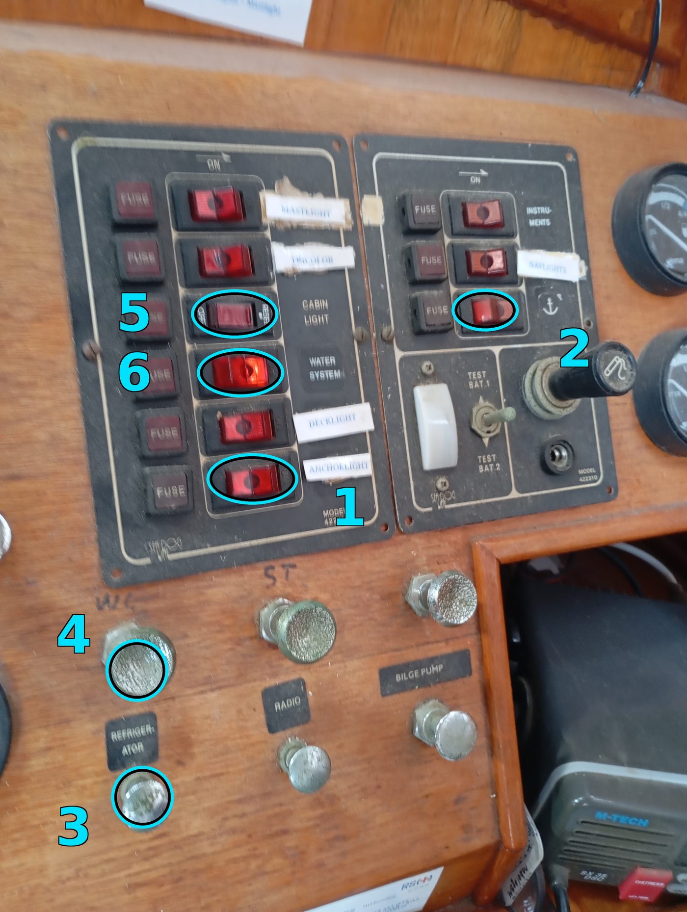 The two breaker panels at the chart table, with the anchor light, windlass, refrigerator, WC, cabin light and water system switches circled